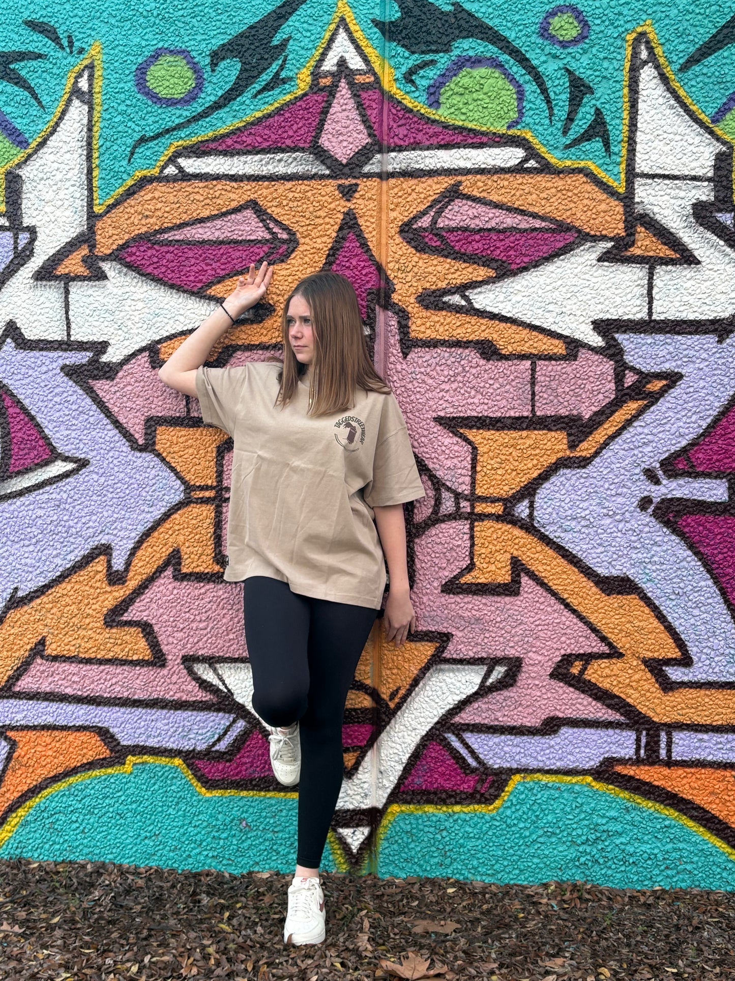 Person posing in front of a colorful geometric mural in taggedstreetwear tee