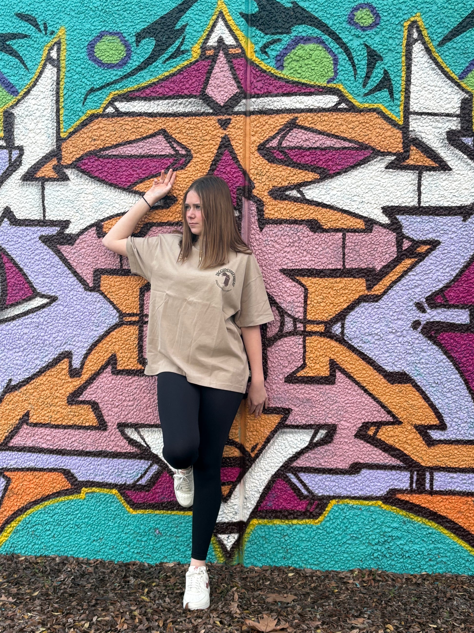 Person posing in front of a colorful geometric mural in taggedstreetwear tee